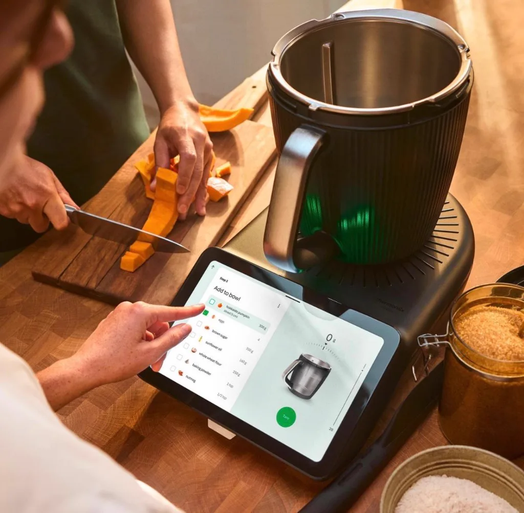 Thermomix touchscreen showing a guided recipe with ingredients being weighed in the bowl