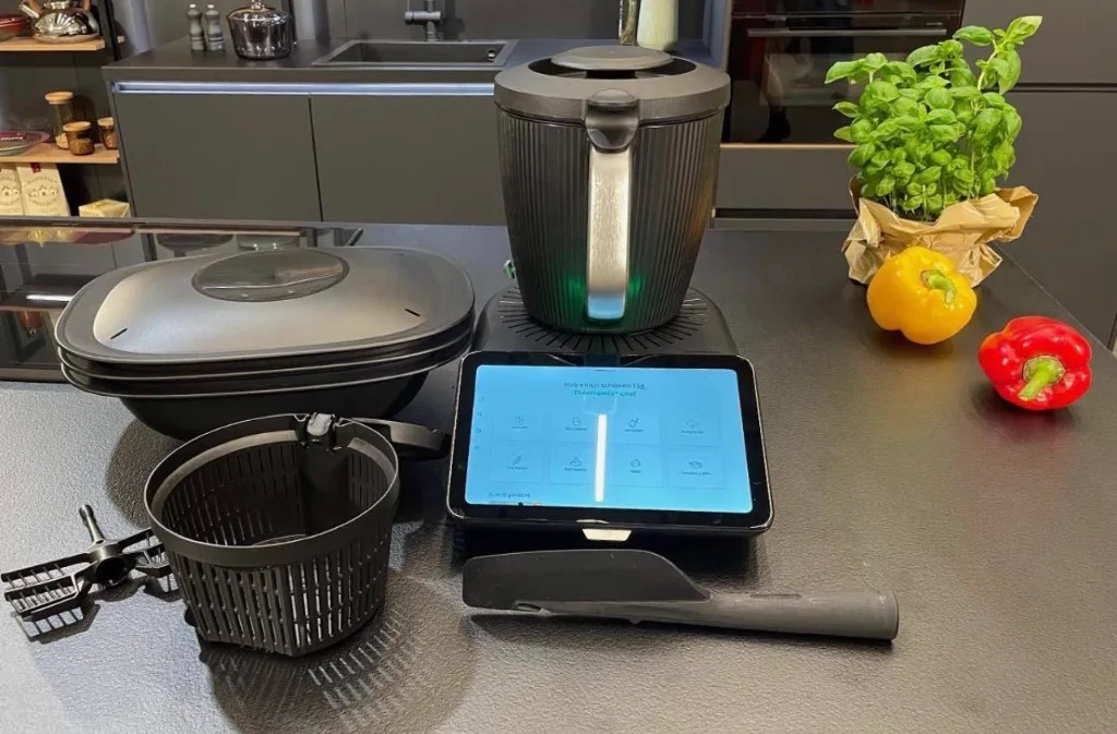 Thermomix with Varoma steamer basket, whisk and spatula on a kitchen island